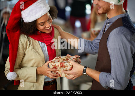 Festa di Natale in compagnia.popolo sorridente in santa hat Natale dando presen Foto Stock