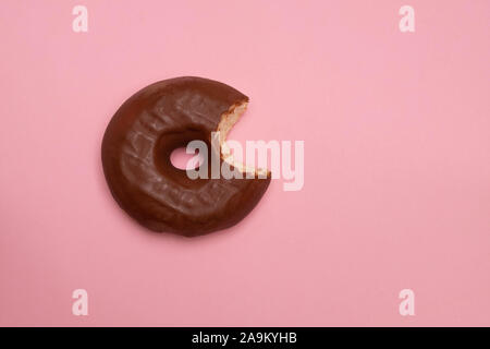 Delizioso morso ciambella con glassa di cioccolato su soft rosa sullo sfondo della carta Foto Stock