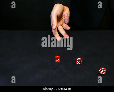 L'uomo getta dadi rossi su una tavola nera superficie, concetto di casinò Foto Stock