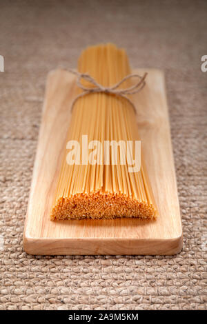 Italian spaghetti legati in mazzi da corda artigianale giacente sul naturale piatto in legno Foto Stock