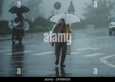 Sapa, Vietnam - 13 Ottobre 2019: Un vecchio uomo asiatico sotto un ombrello si allontana dalla telecamera sotto la pioggia battente nella piccola città di sapa Foto Stock