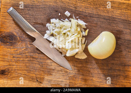 Tagliate a fette le cipolle a dadini su un tagliere di legno con un coltello di cuochi e una metà o metà bianco Sbucciate la cipolla di cottura Foto Stock