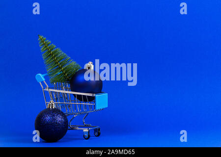 Mini carrello con piccolo albero di Natale e la marina natale decorazione ninnolo palle su sfondo blu Foto Stock