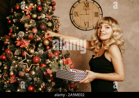 Allegro sorridente donna bionda decora albero di Natale con le palline. Il tempo di Natale. Happy Holiday. Albero di natale. Nuovo anno sorpresa presente Foto Stock