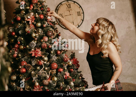 Allegro sorridente donna bionda decora albero di Natale con le palline. Il tempo di Natale. Happy Holiday. Albero di natale. Nuovo anno sorpresa presente Foto Stock