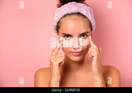 Una bellissima ragazza con una benda sul suo capo contiene patch sotto i suoi occhi mentre in piedi su un sfondo rosa. Foto Stock