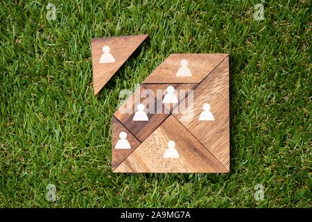Vista aerea del quadrato Tangram blocco di legno con figure umane sul tappeto erboso verde sullo sfondo Foto Stock