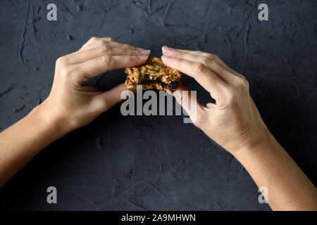 Dieta o cibo vegan concetto. Donna slanciata mani tenendo i fiocchi d'avena colazione cookie sandwich con il cioccolato scuro su sfondo nero spazio copia Foto Stock