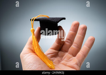 Close-up di mano di una persona in miniatura di contenimento della graduazione nera Hat con fiocco giallo Foto Stock