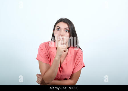 La donna che mostra un segno di silenzio gesto mettendo il dito in bocca su bianco Foto Stock