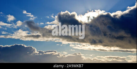 Il sole, oscurato dal passaggio di un cumulo nimbus cloud, getta sunray fino a raggiungere il blu del cielo. Foto Stock