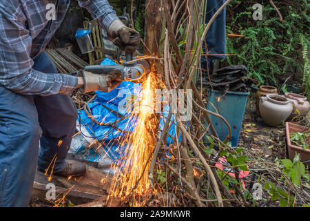 L'uomo utilizzando una smerigliatrice angolare lavora in giardino con scintille volanti. Il taglio di pericoloso vecchi chiodi da un post. Foto Stock