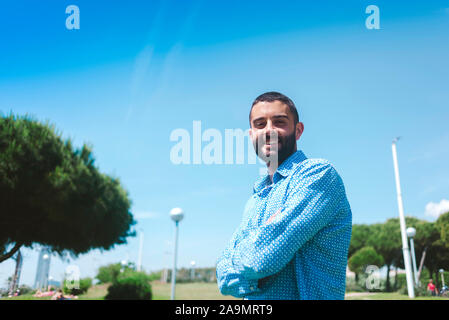 Giovane uomo sorridente e in piedi con le braccia incrociate Foto Stock