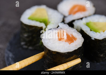 Sake Giapponese maki roll con salmone e avocado, bacchette di legno tenendo un rotolo Foto Stock