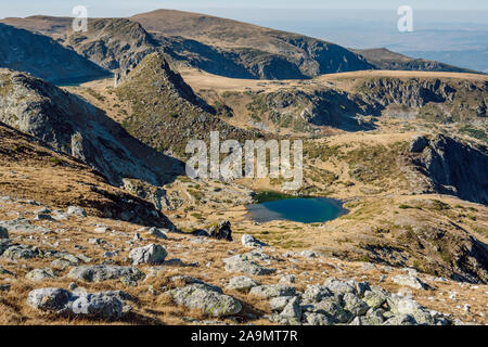 Splendido paesaggio montano con un piccolo lago dalle acque blu, circondato da prati con erbe secche d'autunno giallo, Monte Rila, Bulgaria. Foto Stock