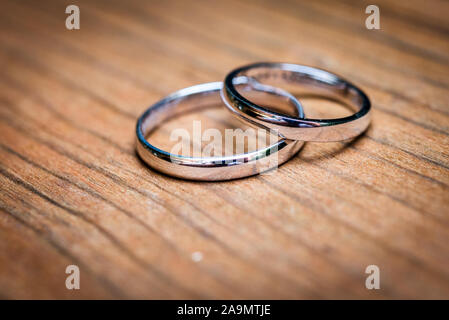 Gli anelli di nozze layingon in legno naturale di un tavolo o di una scrivania. Sposa e sposi argento o oro bianco weddingrings naturale su una superficie di legno. Close up foto. Foto Stock