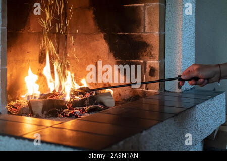 Mano femmina si raddrizza la combustione di legna da ardere con un poker di ferro in un caminetto aperto e dal carbone fly bella scintilla. Il calore e il comfort in un ambiente accogliente Foto Stock