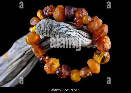 Close up di un greggio ruvida naturale ambra bracciale con diverse tonalità di arancio avvolto attorno al vecchio ramo di legno con sfondo nero e concentrarsi per Foto Stock