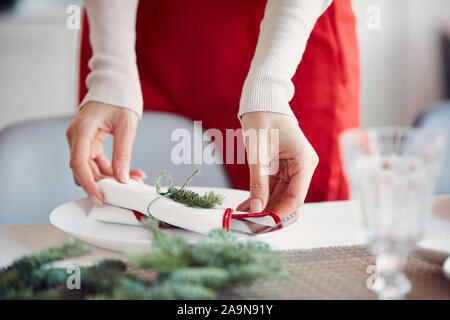 Close up riconoscibile giovane donna la piegatura di tovaglioli durante l'impostazione della tabella per il banchetto di Natale e la decorazione elegante sala da pranzo, spazio di copia Foto Stock
