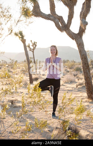 Giovane donna felice giocando lo yoga ed esprimendo fitness generale nei ritratti. Deserto Mojave Joshua Tree, CA USA Foto Stock