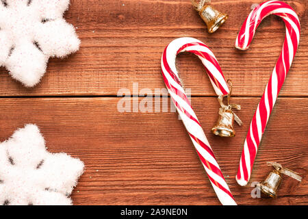 Natale flatlay: bianco soffici fiocchi decorativi e due strisce di colore bianco e rosso di canna di caramelle con tre campane d'oro su sfondo di legno. Vista dall'alto, Foto Stock