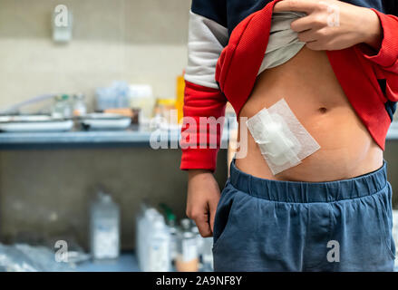 Giovane ragazzo adolescente in ospedale. Bambino con taglio avvolto nel gabinetto medico in ospedale. Kid mostra ventre ferita. Concetto per ferita dalla chirurgia. Foto Stock