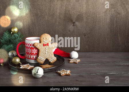 Composizione di natale con Gingerbread cookie e bevanda calda su sfondo di legno, copia dello spazio. Gingerbread Man e la tazza di tè, cacao. Foto Stock