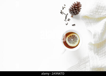 Accogliente winter composizione - tazza di tè con limone, bianco caldo maglione, pigna e asciugare le foglie di tè isolati su sfondo bianco. Minima concep invernale Foto Stock