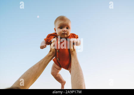 Infant baby essendo trattenuto in alto nel cielo da padre mani outdoor adorabile bambino felice famiglia lifestyle papà e figlia kid giocare insieme Foto Stock