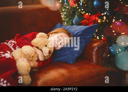 Piccola ragazza dorme vicino accesa albero di natale Foto Stock