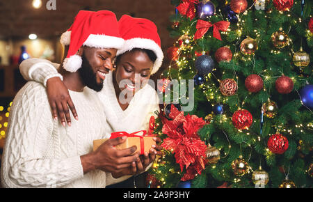 Ritratto di felice afro giovane azienda dono e di stare vicino a albero di Natale Foto Stock
