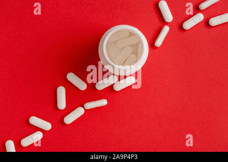 Pillole di bianco su sfondo rosso. bianco di plastica bottiglia di medicina. Vista superiore Foto Stock