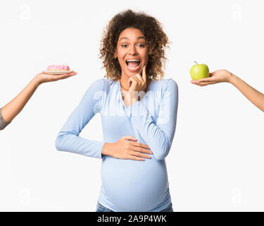 Gravidanza La nutrizione. Emotional donna incinta scegliendo tra apple e ciambella Foto Stock