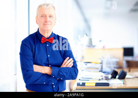 Ritratto di imprenditore senior indossando il filtro bow tie mentre in piedi con le braccia incrociate in ufficio. Foto Stock