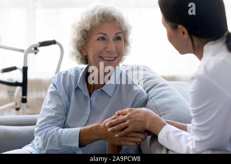Cura l'infermiera aiutando tenendo le mani di felice disabilitato vecchia donna Foto Stock