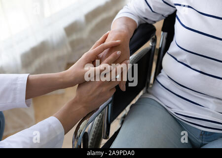 L'infermiera tenere il supporto a mano handicappati senior paziente su sedia a rotelle, primo piano Foto Stock