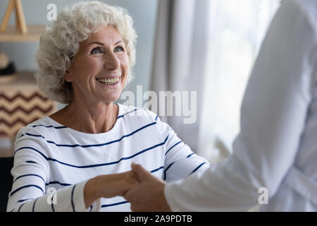 Felice la nonna paziente tenendo mano del caregiver di alzarsi Foto Stock