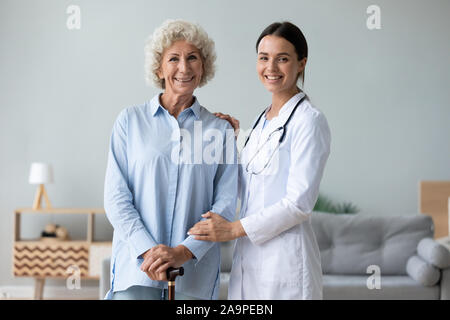 Infermiera femminile aiutando vecchia donna tenendo la canna da zucchero guardando la fotocamera Foto Stock