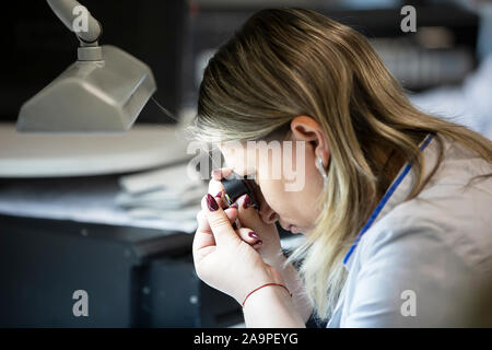 La Bielorussia, la città di Gomil, 24 aprile 2019. Industria dei gioielli. Un worker esamina un diamante in una lente di ingrandimento. Incisore. Foto Stock