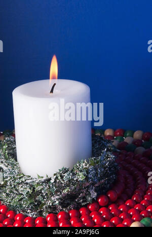 Una masterizzazione christmas candle circondato da coperta di neve verde e perline di legno. Blu sullo sfondo a trama con copia spazio. Foto Stock