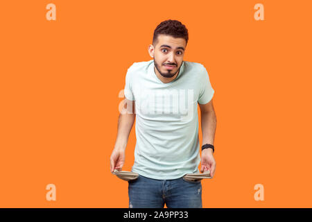 Ritratto di frustrati preoccupato brunette uomo con la barba in casuale t-shirt bianco girando le tasche vuote che mostra non ho soldi gesto, bancarotta. in Foto Stock