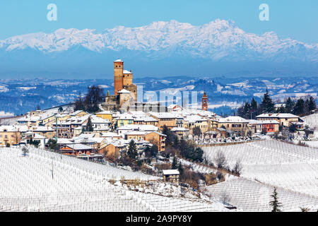 Piccola città medievale e vigneti sulle colline coperte di neve come le montagne sullo sfondo in Piemonte, Italia settentrionale. Foto Stock