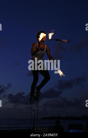 Intrattenitore di strada giocolando bastoni di fuoco su un monociclo ad una folla in Mallory Square Key West Florida Foto Stock