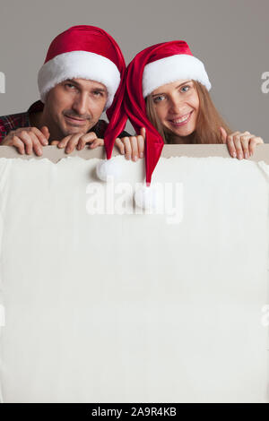 Coppia felice in cappelli di Babbo Natale azienda intestazione vuota con lo spazio di copia Foto Stock