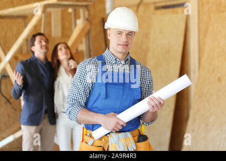 Caposquadra con casa piani di progettazione e di giovani entusiasti coppia al sito in costruzione Foto Stock