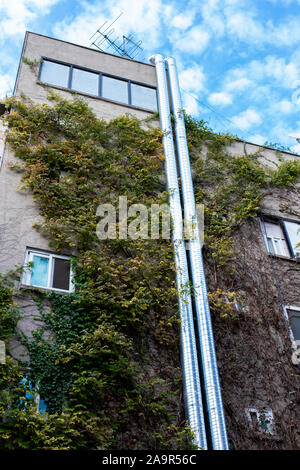 Il giardinaggio verticale con impianti di tessitura. Le pareti coperte di edera. Tubi lungo la parete fino al tetto. Antenna sul tetto sotto il blu cielo molto nuvoloso Foto Stock