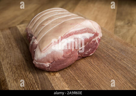 Una chiusura di un grezzo di taglio di carne chiamato una spalla di maiale legato e rullato con macelleria stringa con la sua pelle rigata pronto per il crepitio su una tavola di legno b Foto Stock