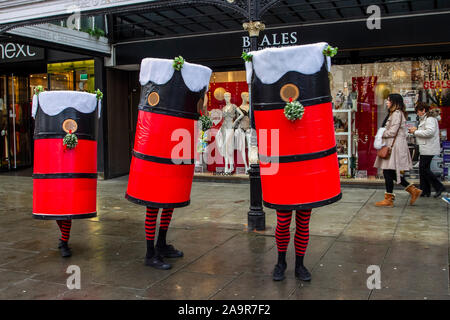 Gruppo di intrattenimento natalizio "The Funnels" all'evento di accensione delle luci natalizie organizzato nel centro della città come parte del programma di miglioramento DELLE OFFERTE. Carbuncle, Adams e Cognac pop up da dentro rosso e nero grandi tubi per interagire con la folla, questo divertente trio vittoriano poi invitare il pubblico a partecipare con i loro giochi, divertimento e frivolity. Foto Stock