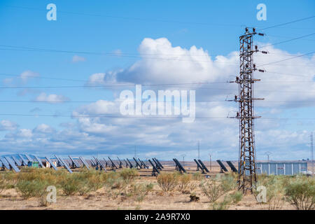 I pannelli solari con tracker di campo generano energia sostenibile con un albero elettrico in primo piano per il trasporto di elettricità generata, Foto Stock