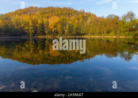 Acqua fresca lago in una ex cava con riflessioni dell'estate indiana e i colori autunnali delle foglie su un inizio di mattina di novembre Foto Stock